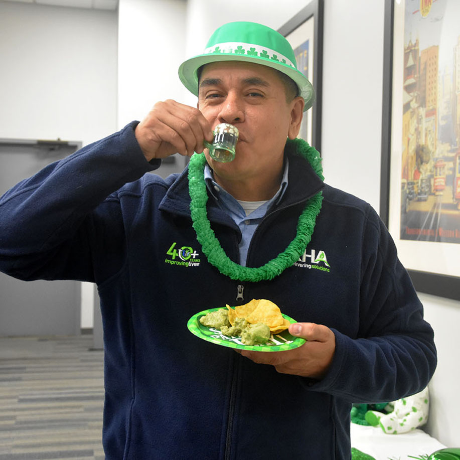 A Man Wearing A Green Hat St. Patrick’s Day Hat, Holding A Plate Of Food And Drinking From A Small Cup