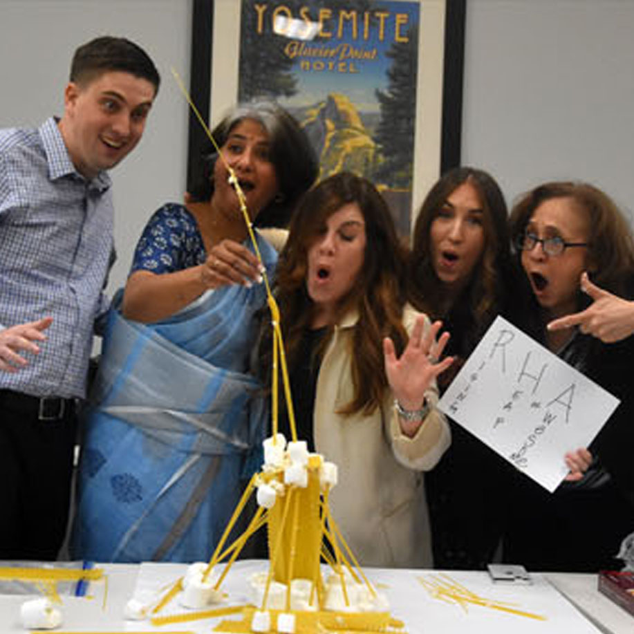 A Group Of People Using Marshmallows And Noodles To Build A Tower